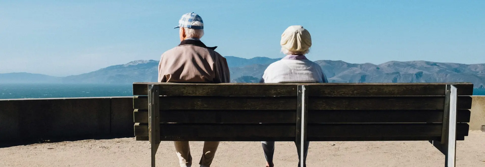 man and woman sitting on bench facing sea
